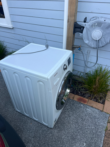 White washing machine next to a wall-mounted water connection.