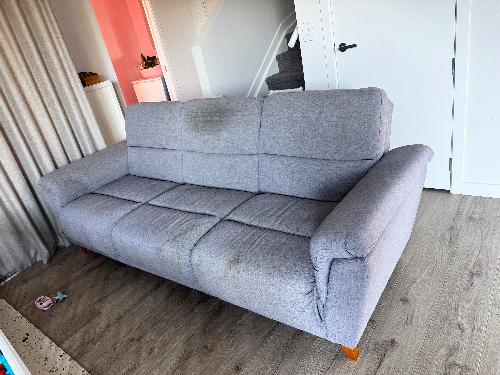 Gray fabric sofa with visible stains and wooden legs.
