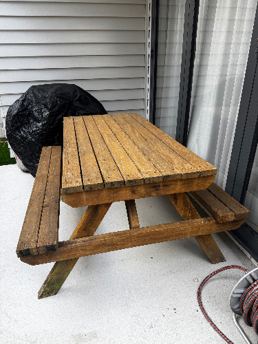 Wooden picnic table with metal fittings and a black cover nearby.
