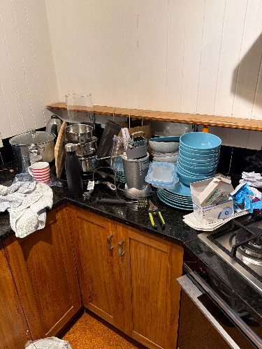 Cluttered kitchen counter with dirty dishes, blue plates, cookware, utensils, and a coffee maker.