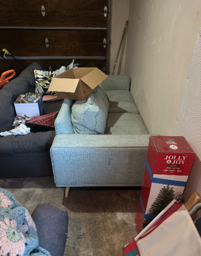 Light blue sofa, cardboard box, red and blue holiday packaging with a Christmas tree image, assorted items in boxes.