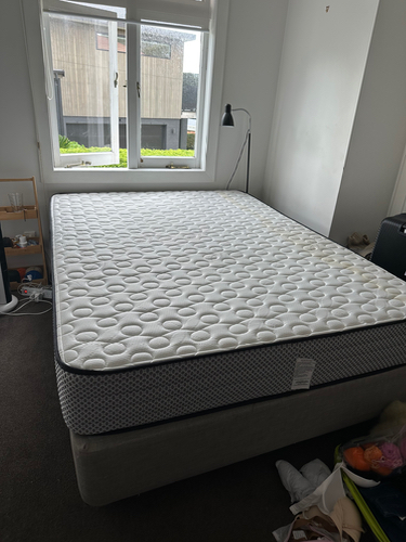 A white mattress on a gray bed frame with a floor lamp nearby.