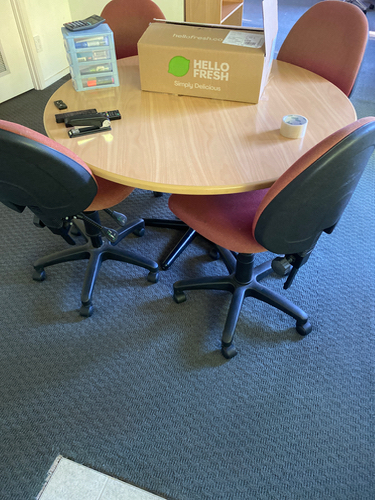Round wooden table, four red rolling chairs, Hello Fresh box, transparent tape dispenser, black markers.
