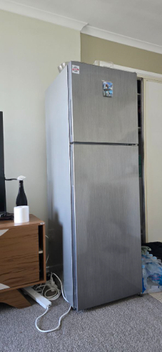 Stainless steel refrigerator, wooden side table, black bottle.