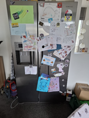 Stainless steel refrigerator covered in colorful drawings, stickers, and papers.