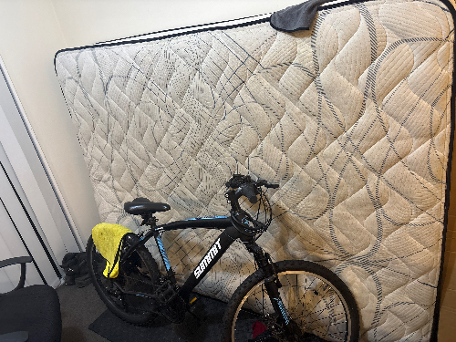 Black bicycle and mattress leaning against a wall.