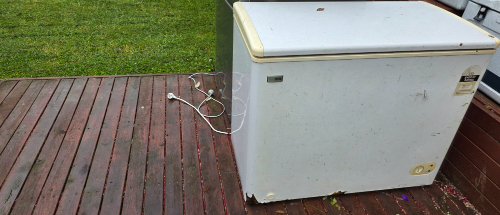 White chest freezer with power cord on wooden surface.