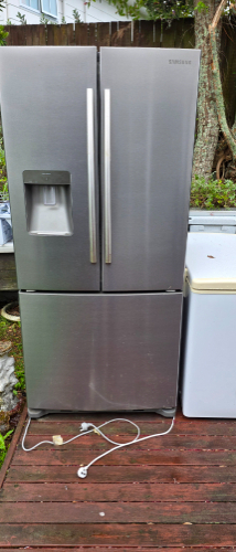 Stainless steel refrigerator with French doors and ice/water dispenser, adjacent white appliance.