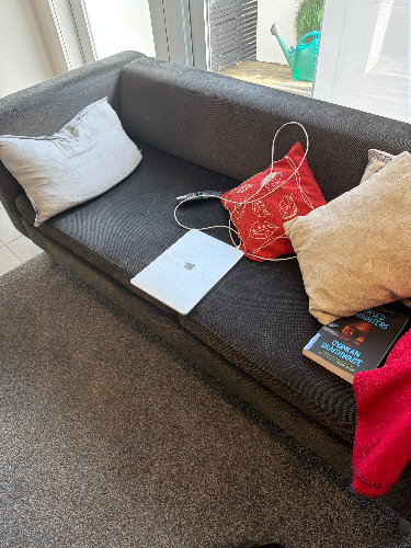 Sofa with two cushions, red bag, laptop, and books.