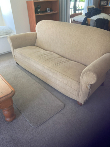 Beige sofa with curved arms and wooden legs, beige rug beneath it, wooden coffee table.