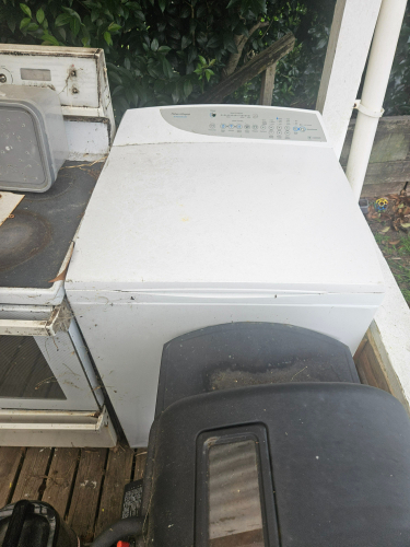 White top-loading washing machine and black lawn mower.