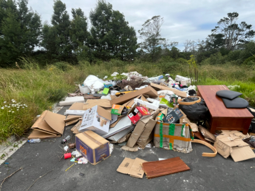 Pile of assorted garbage including cardboard boxes, plastic bags, furniture, and miscellaneous waste.