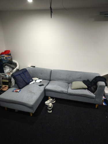 Gray sectional sofa with a blue bag, white sneakers, and a green cushion.
