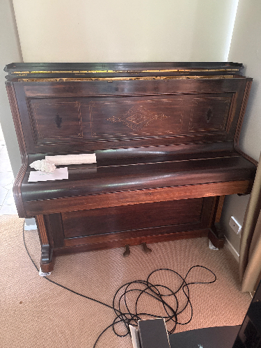 Wooden piano with sheet music and a rolled document on top.