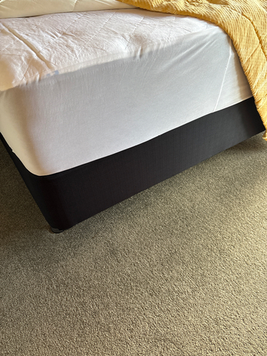 Bed with a black bed skirt and white mattress, partially covered by a yellow blanket.