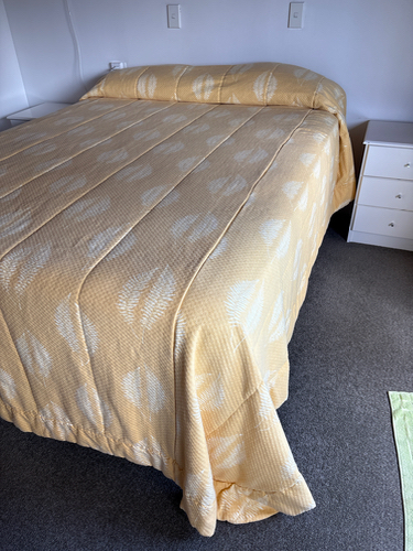 Yellow quilted bedspread on a bed, white nightstand beside the bed.