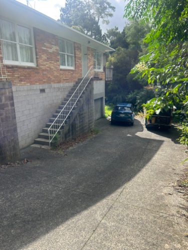 Two cars parked in a driveway, a brick house with stairs leading up to it.