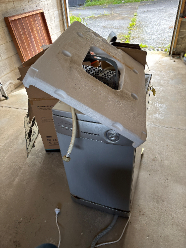 Washing machine with a detached lid and exposed hoses.