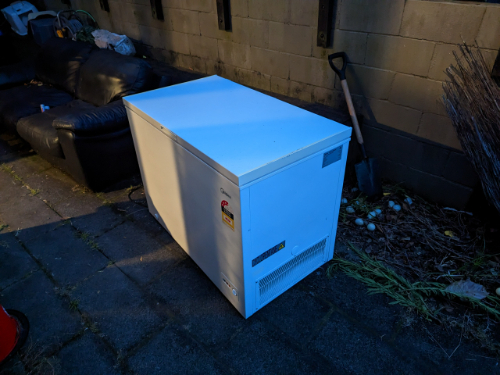 White chest freezer, black leather couch, shovel, and bundle of dried twigs.