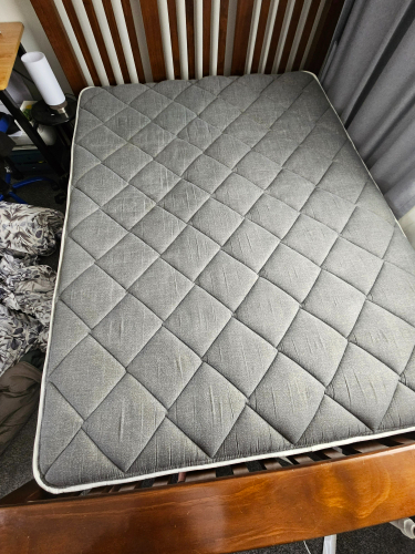 Gray quilted mattress on a wooden bed frame.