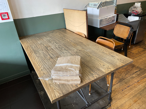 Wooden table with stacked brown paper and four chairs.