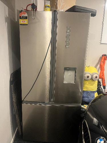 Stainless steel refrigerator with water dispenser, minion plush toy, BMW logo.