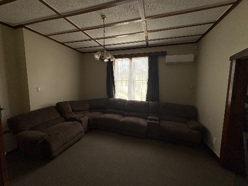 L-shaped brown sectional sofa, ceiling fan, window with curtains, air conditioning unit, doorframe.