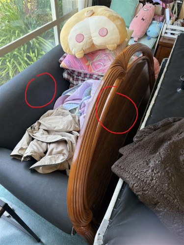 A brown wooden headboard, a pile of colorful blankets, a beige jacket, and a large plush toy with facial features.