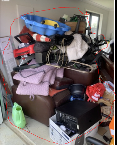 Cluttered pile of furniture, plastic containers, cushions, gardening tools, and miscellaneous items.