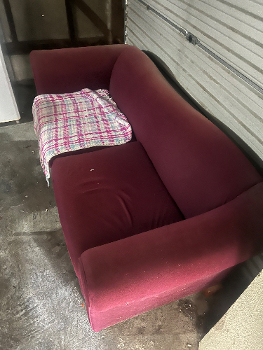 Maroon couch with a plaid blanket.