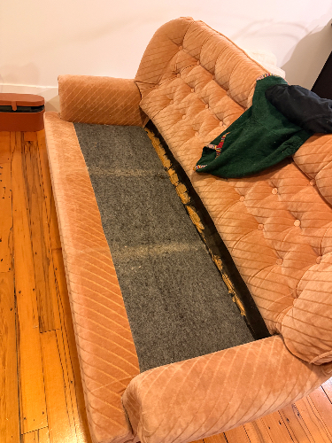 Pink couch with a frayed area and a green sweater draped over it.