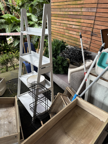 White ladder shelf, white plates, black wire basket, wooden crates, cleaning supplies.