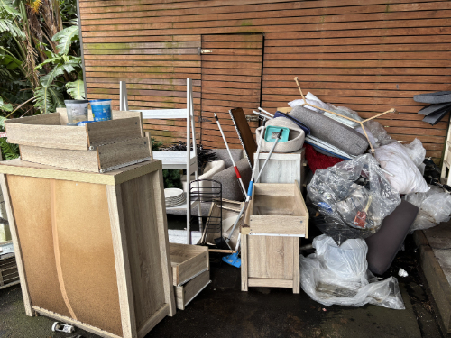 Wooden furniture pieces, garbage bags, cushions, cleaning supplies, and a stack of assorted items.