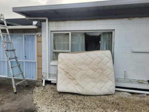Ladder, mattress against wall, window with curtains.