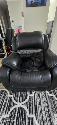Black reclining chair with a gray pillow and a black blanket draped over it.