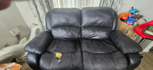 Black leather loveseat with a tear and worn upholstery.