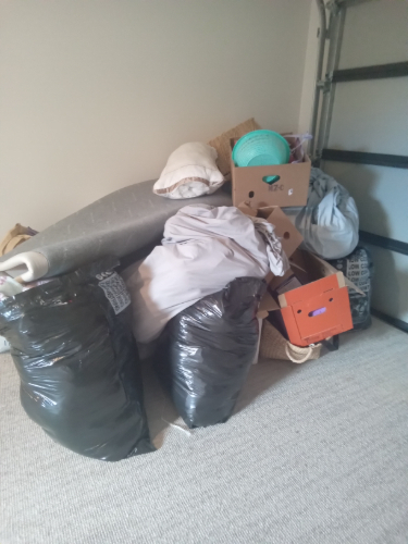 A pile of black garbage bags, a rolled rug, storage boxes, blankets, and a green basket.