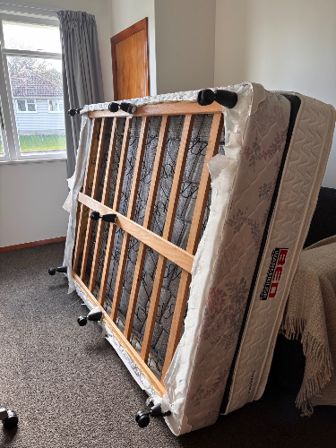 Folding mattress on a wooden frame with wheels.