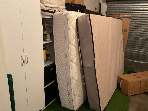 Two stacked mattresses, one white quilted and one beige.