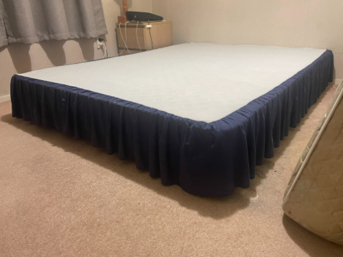 A bed with a navy blue dust ruffle and a white mattress.