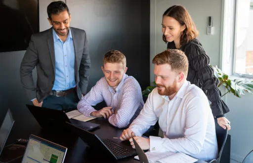 Four young professionals collaborating around a table with laptops and documents in a modern office.