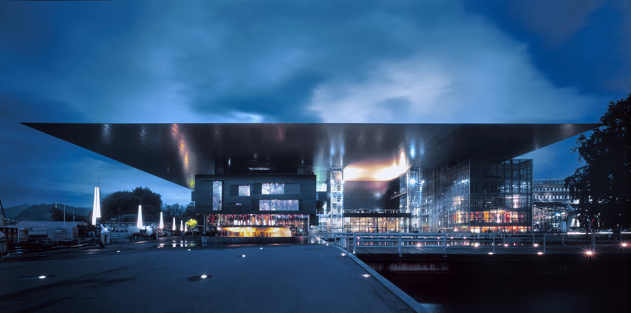 Modernes Gebäude mit grossem überhängendem Dach und beleuchteter Glasfassade nachts.