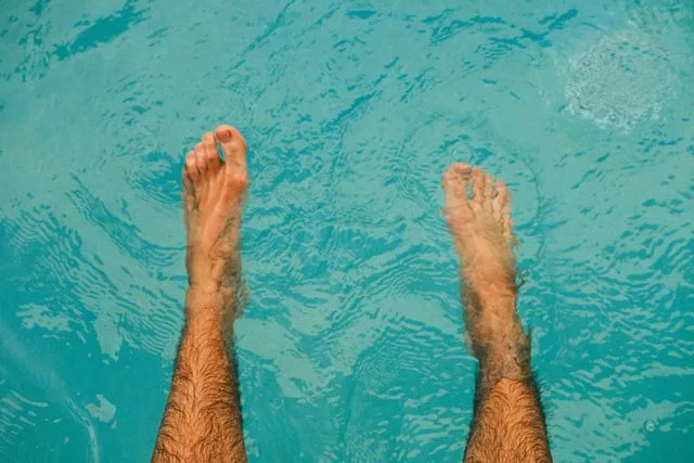 Feet soaking in a swimming pool to illustrate toenail fungus prevention.