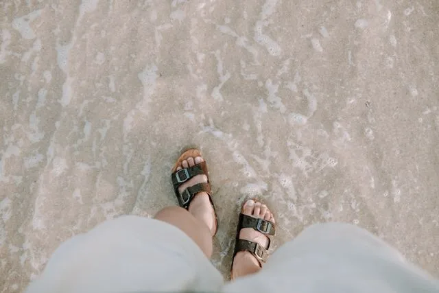 Person wearing sandals while walking on a sandy surface.
