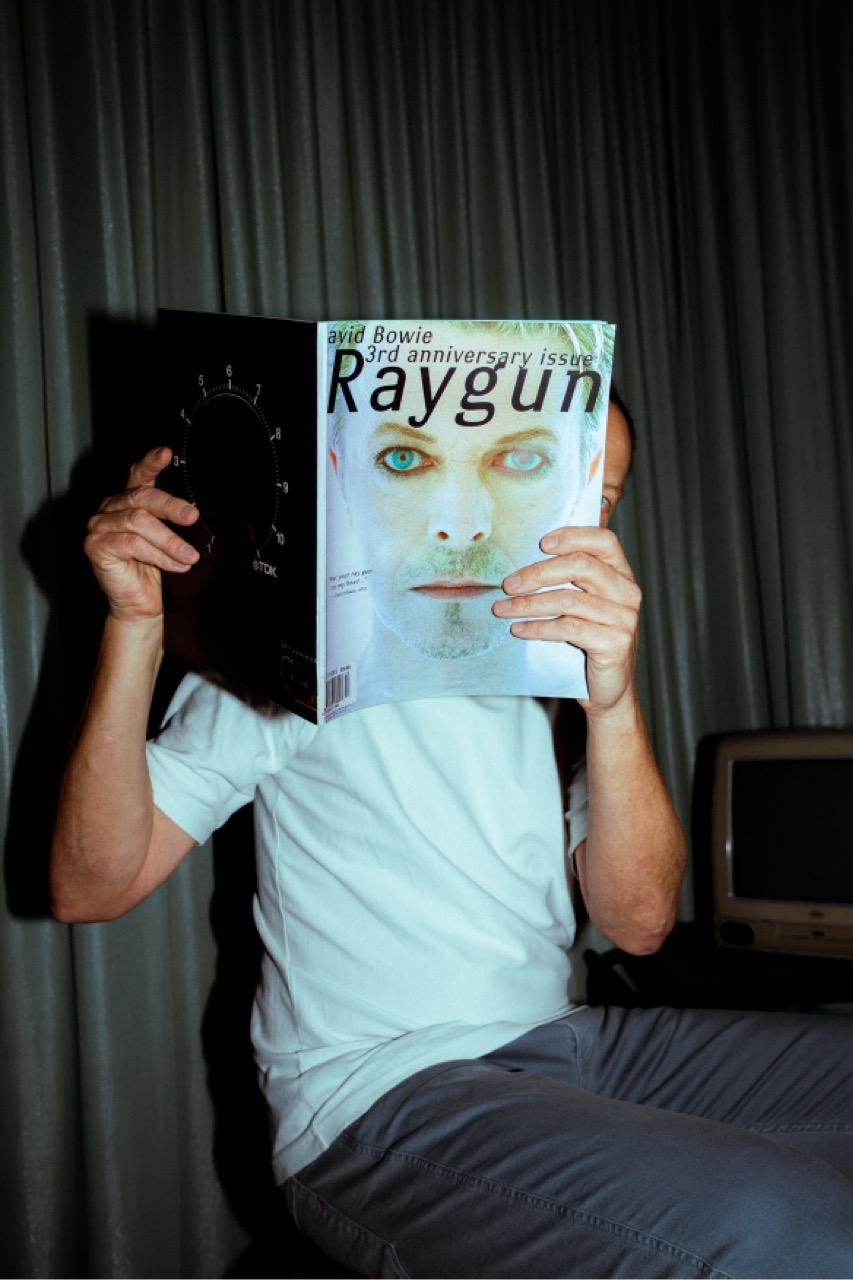 Robert hält sich ein Magazin mit David-Bowie-Cover vors Gesicht, in der anderen Hand ein altes Kassettenradio.