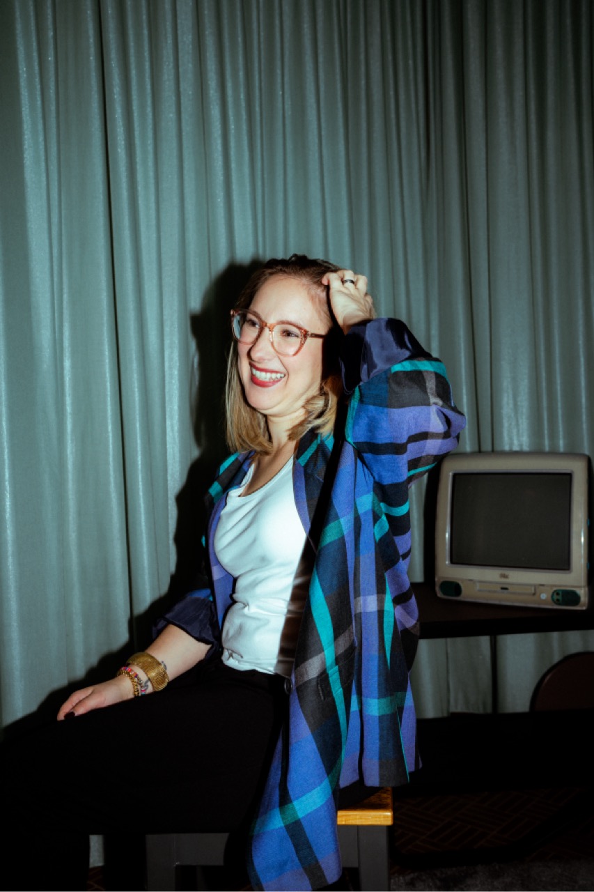 Nancy lachend im karierten Flanellhemd, im Hintergrund ein bauchiger iMac G3.
