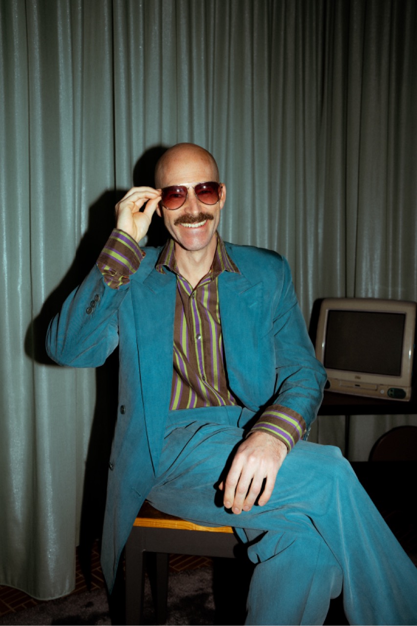 Michi im türkisfarbenen 70er-Jahre-Anzug mit getönter Sonnenbrille und Schnurrbart.
