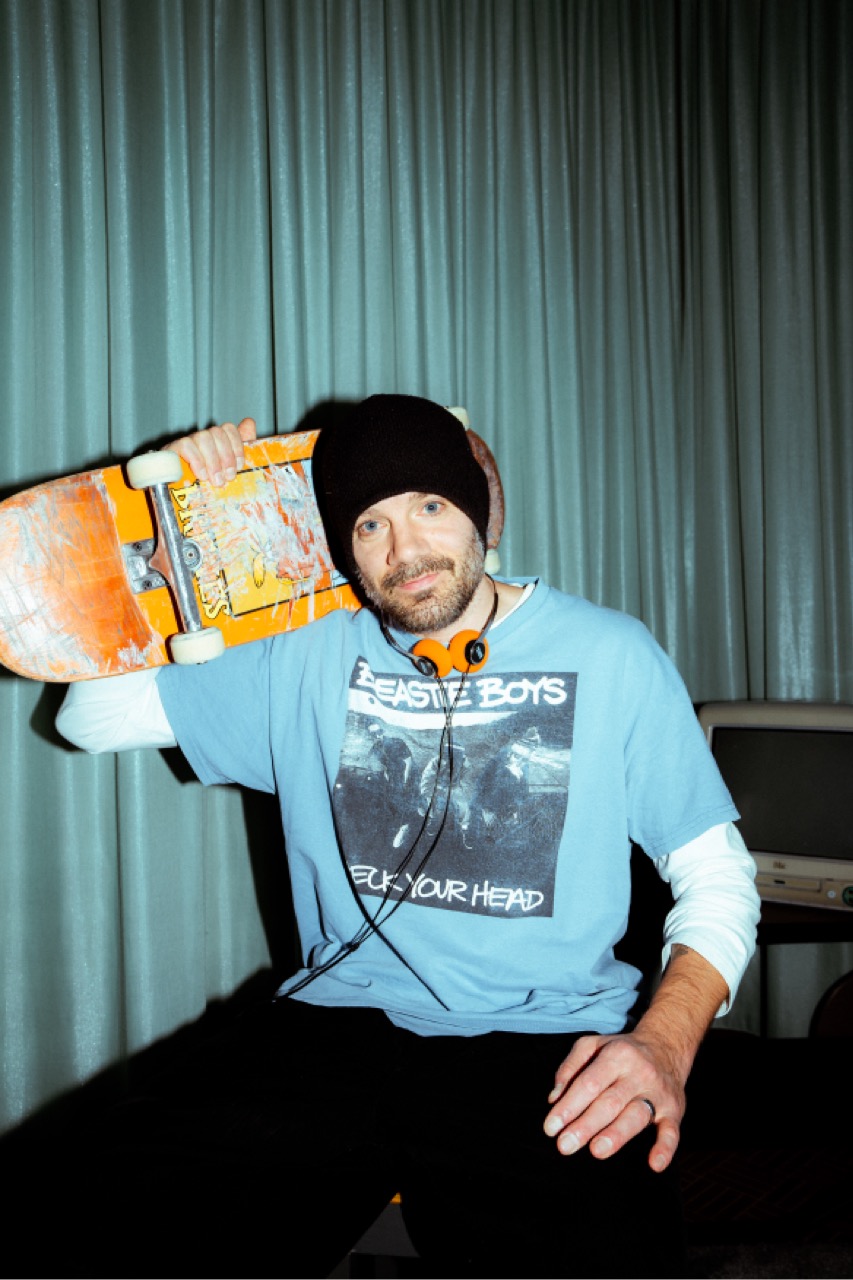 Fredi mit Mütze und Beastie-Boys-Shirt, ein Skateboard über der Schulter.
