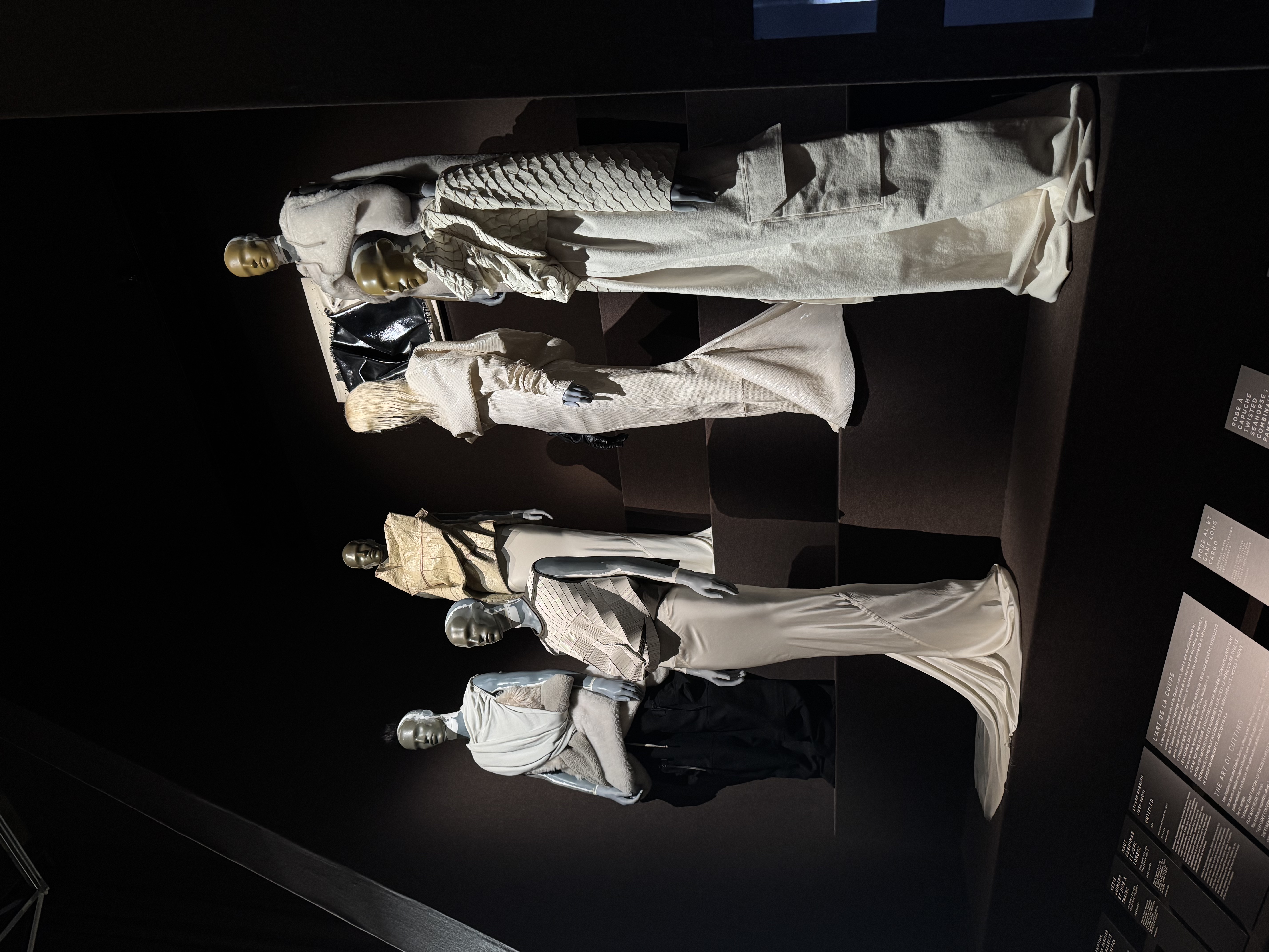 Modeausstellung mit mehreren Schneiderpuppen in cremefarbener Avantgarde-Mode auf abgestuften Podesten.