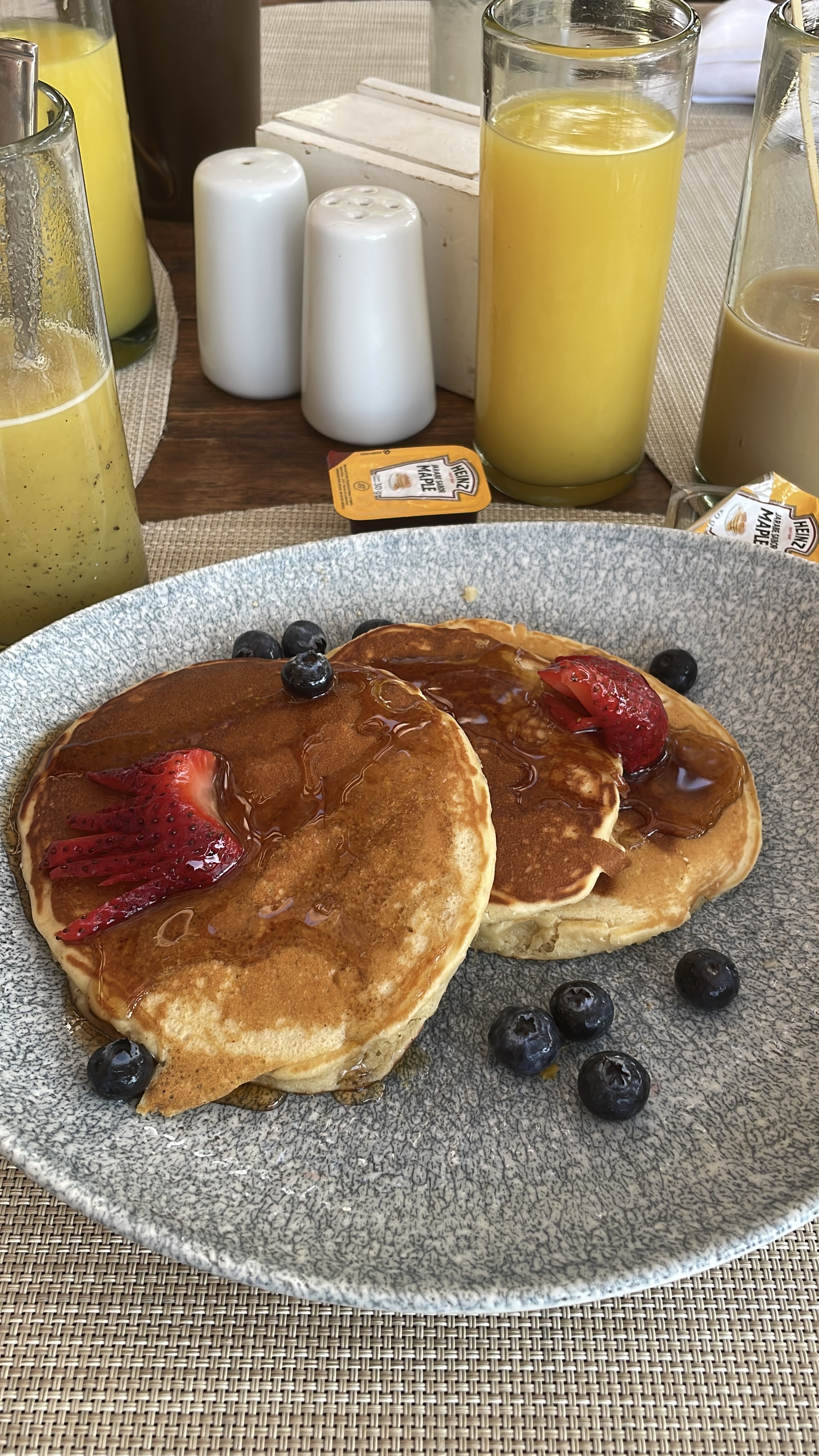 Zwei Pancakes mit Erdbeeren, Heidelbeeren und Ahornsirup auf einem Teller, im Hintergrund Orangensaft.